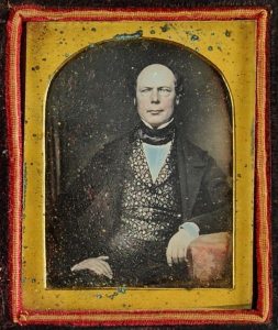 Tinted daguerreotype portrait of a middle-aged man in a patterned vest, early 1850s.