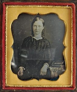 Daguerreotype of a young woman posed beside a table with books, c.1855.