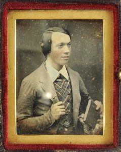 Tinted daguerreotype portrait of a young man holding a daguerreotype case, 1845-48.