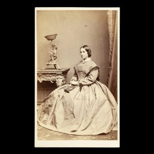 Studio portrait of young woman in a fine dress, holding a carte de visite album. Melbourne, c.1865.