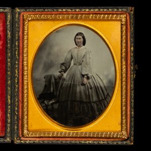 Ambrotype of a woman standing beside a chair draped with clothing. (New South Wales?), c.1863.
