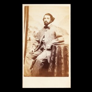 Portrait of a dapper gentleman in bow-tie and grey flannel suit, seated in front of a painted backdrop. Melbourne, c.1867.