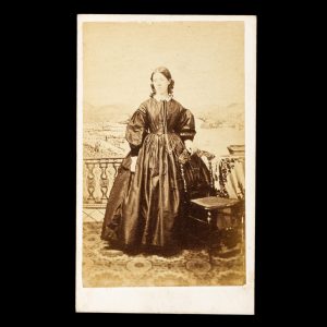 Young woman posed in front of a painted studio backdrop of Otago Harbour. Dunedin, New Zealand, 1863-65.