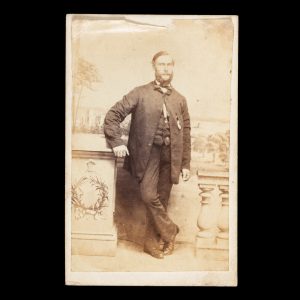 Studio portrait of a gentleman posed before a painted backdrop with a view of Government House and Sydney Harbour. Sydney, c.1864.