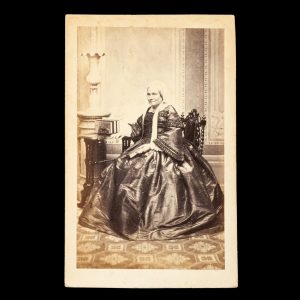 Studio portrait of a wealthy lady in a fine taffeta dress, holding a photograph album. Sydney, early 1860s.