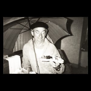 Charles Blackman in London with umbrella, holding ‘English picnic’, 1981