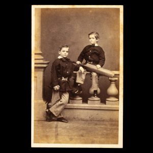 Studio portrait of two identically dressed young brothers, one holding a cricket bat. Sydney, 1864-5.