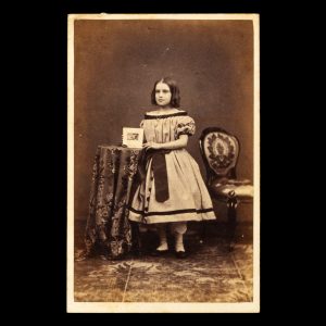 Studio portrait of a young girl holding a carte de visite album. Sydney, 1864-5.